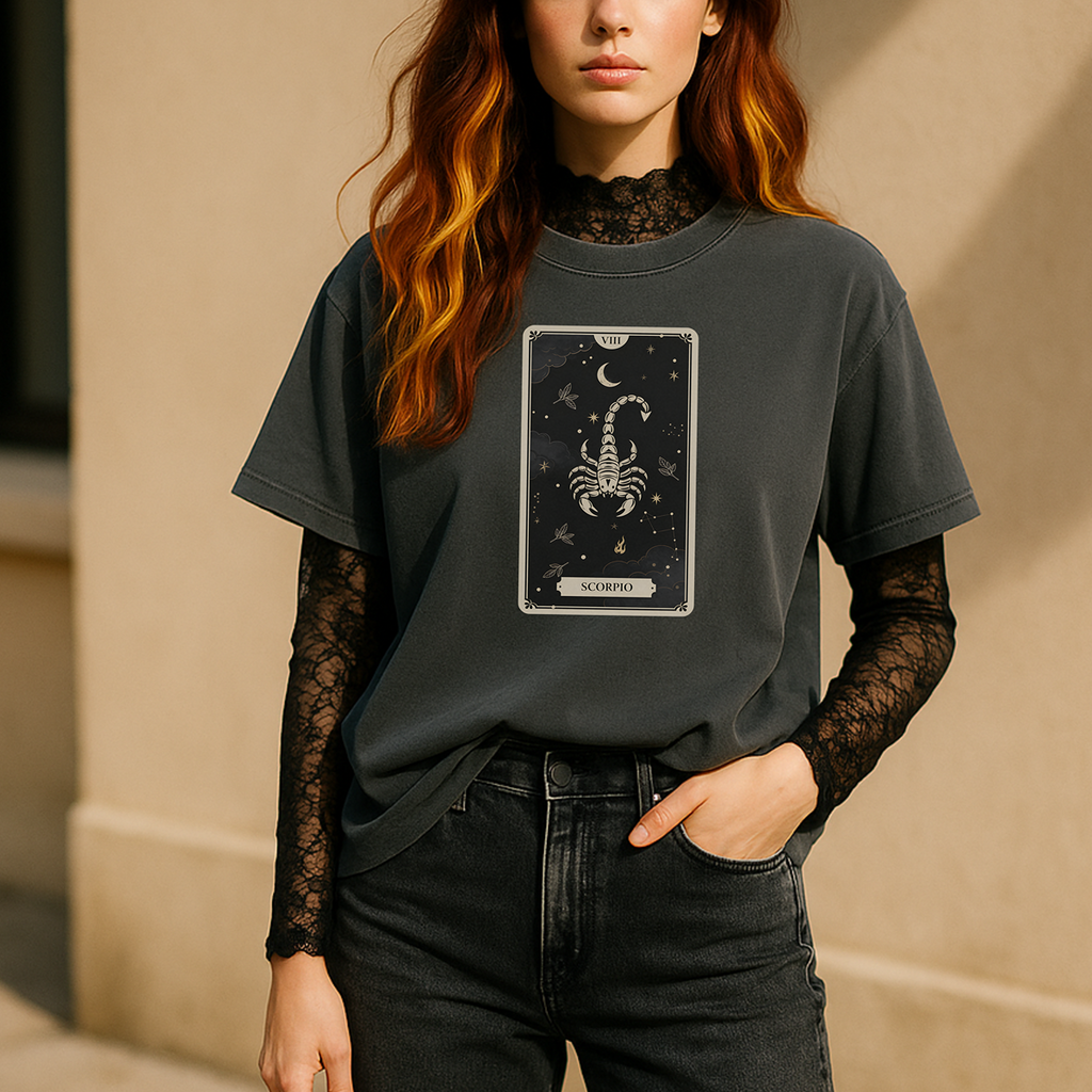 Person wearing a dark gray t-shirt with a scorpion zodiac symbol design, standing against a beige wall.